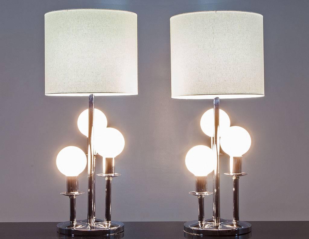 These are unique modern table lamps, made in America, circa 1970s. They consist of a round polished chrome plinth base with three graduated pedestals holding large globe bulbs. The lamp combines futuristic design with the traditional concept of a