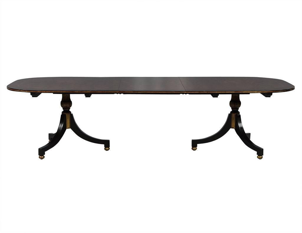 This Regency style dining table is a real beauty. The top is composed of a swirl mahogany field with ebony and boxwood banding finished in a medium walnut stain. It sits atop double Duncan Phyfe style pedestals finished in satin black lacquer with