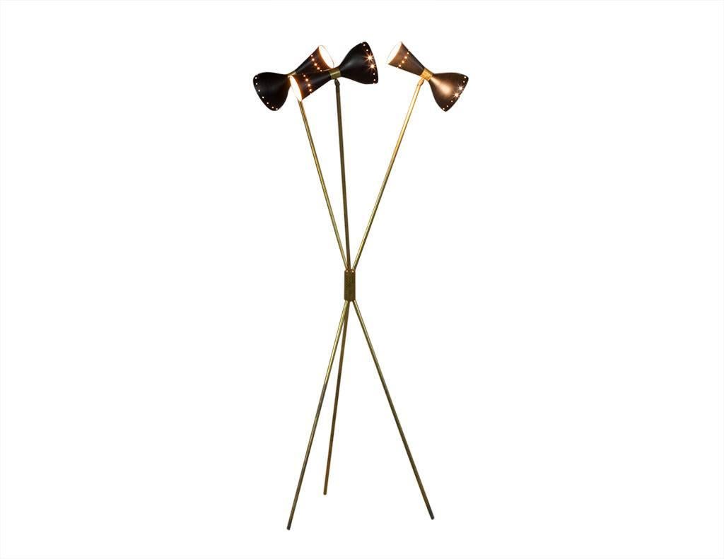 This Modern floor lamp hails from Italy. A Carrocel Original, it is in excellent condition and shows great patina. It is composed of brass tripod legs joined in the middle with adjustable metal rods holding the black metal lampshades with two light