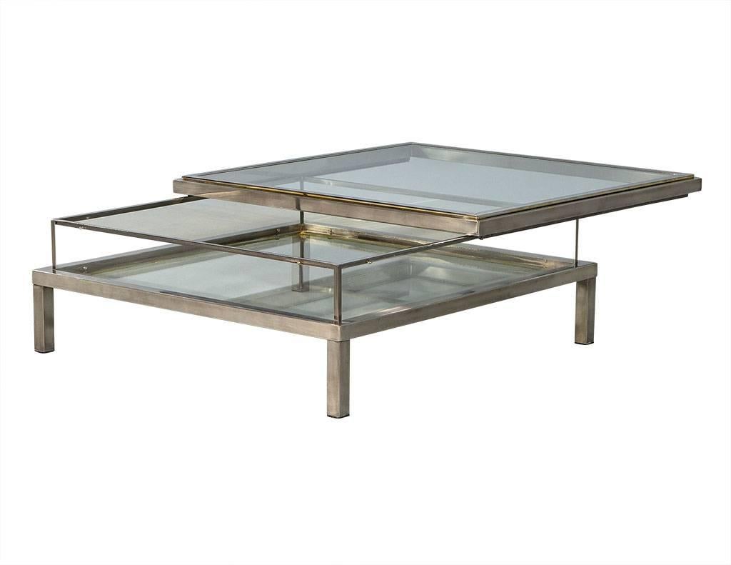 Vintage Italian sliding top stainless steel cocktail table. Featuring large square glass and stainless steel frame, raised on four block legs. Sliding top surface over enclosed glass display case, perfect for featuring artwork, books and