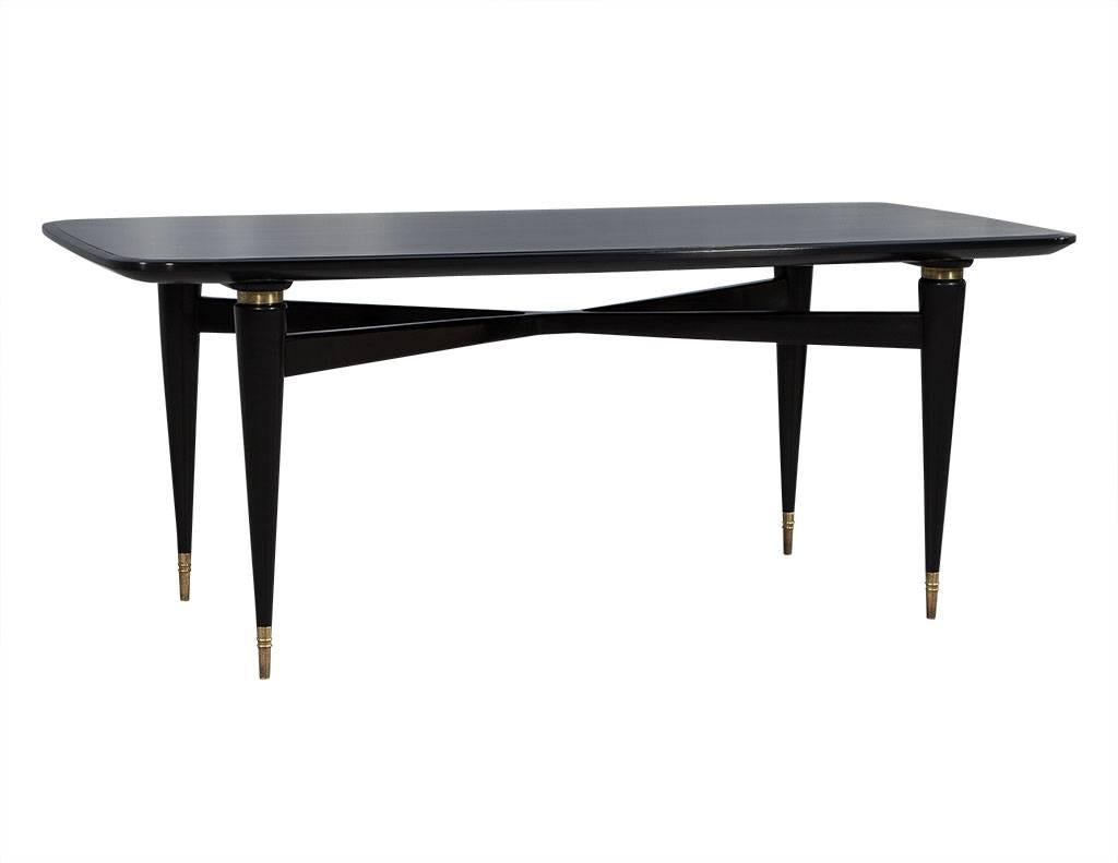 Vintage French black lacquered dining table. Refinished in satin black lacquer, featuring rounded corners and tapered legs connected near the top with X-shaped stretchers. Brass detail rings and leg tips.

Price includes complimentary curb side