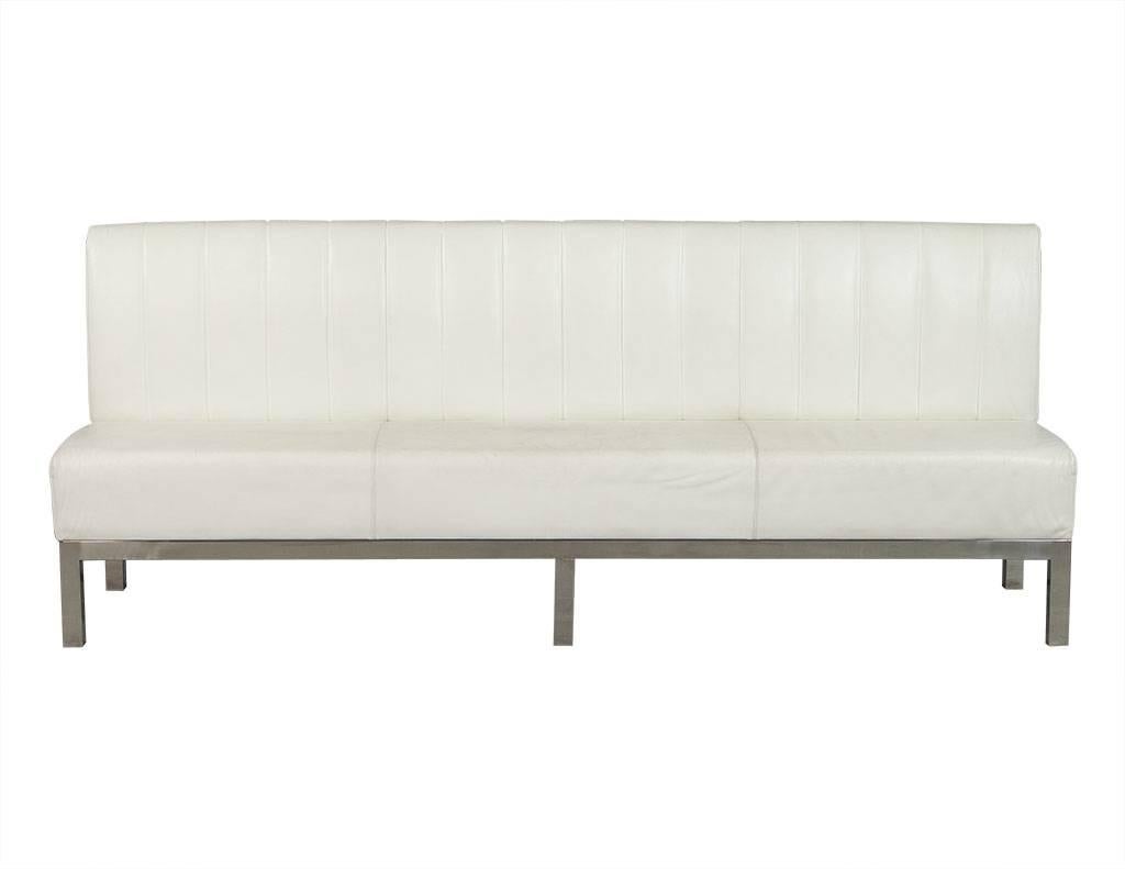 Armless, four-seat white leather banquette with thick, ribbed pattern stitched onto inside back, raised on brushed stainless steel base consisting of six feet.