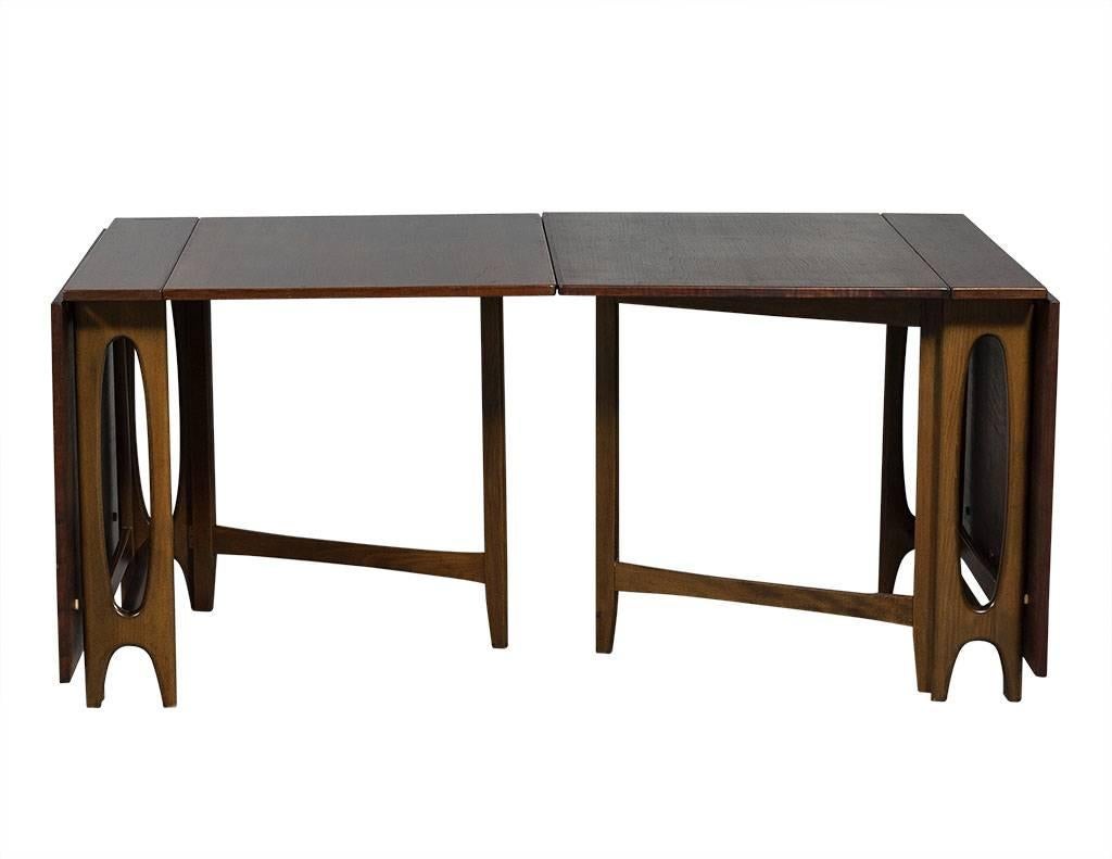 This Mid-Century Modern dining table set is rare and unique. Crafted out of teak wood, it folds into a number of configurations: a one piece console and two consoles which open up into two dining tables. A very practical piece perfect for small