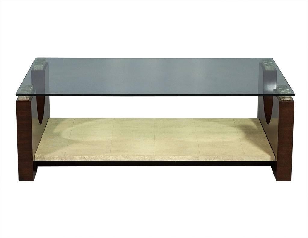 This modern deco style cocktail table is crafted out of rosewood and parchment, this piece has a large glass top and two U-shaped lacquered wood ends with metallic wood pieces for supporting the glass. There is also a large lower shelf with a