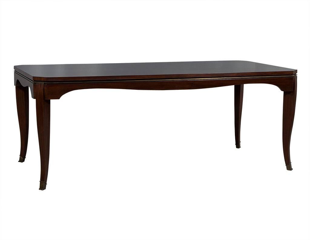 This Art Deco dining table is downright charming. A Carrocel original, it is crafted out of solid wood and has inset brass metal detail around the top and sides as well as angled corners. There is also a black nine inset around the top edge and