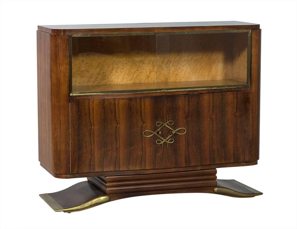 This Art Deco bar cabinet is functional yet ornate. It is a Carrocel Original, with slight wear consistent to age. Hailing from France, this piece is crafted out of gorgeous rosewood with a large curved pedestal base and brass plated front and side