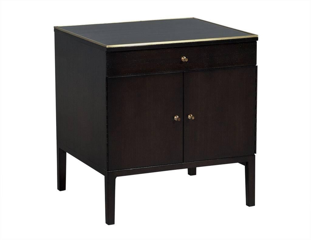 This Mid-Century nightstand is designed by Paul McCobb for The Calvin Group. It is finished in a gorgeous dark brown stain with brass trim on the top edge and brass door knobs to complete the look. Inside the two doors is a neat shelf and at the top