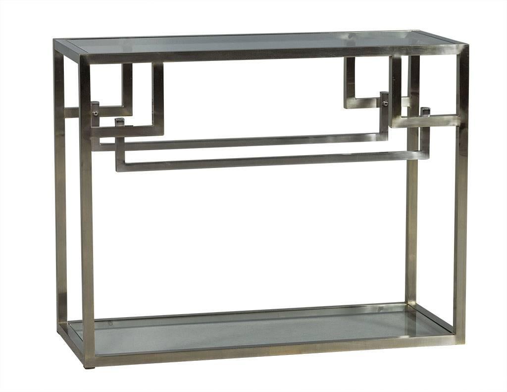This Modern console table is sleek yet detailed. It is composed of stainless steel and glass, with a unique angular design on the front and back. The top and bottom shelves are both glass, and perfect for showcasing trinkets or on its own as a true