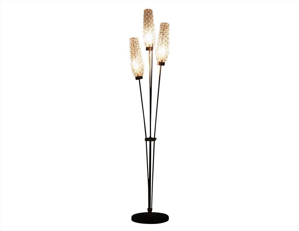 This Mid-Century style floor lamp is designed by Maison Arlus. The frame is crafted out of cast iron and brass, with three crystal glass shades and a round, black base. Arranged in a flower design with three gold stems and one centre wood stem, the