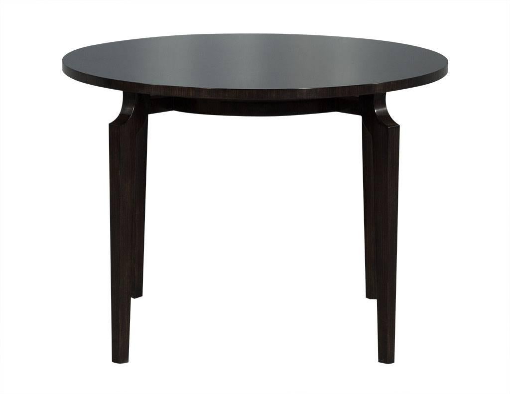 This modern breakfast table is crafted out of fine zebra wood. It has a dark patina, round top, and a radial pattern on the surface. The legs curve as they reach the top, and are connected to a wooden circle right below the table surface. A