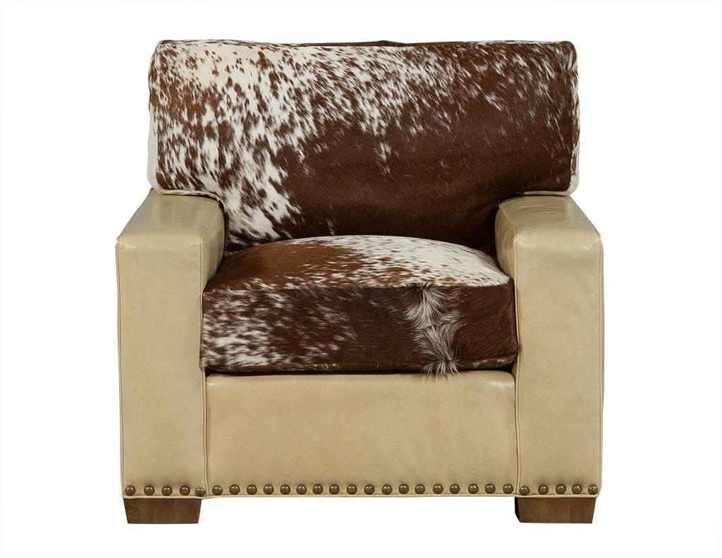 This modern accent chair is quite large and composed of yellowed tan leather with a cowhide seat and backrest pillow to match. The piece sits atop complementary large, square wooden feet, and is a perfect addition to a rustic living room.