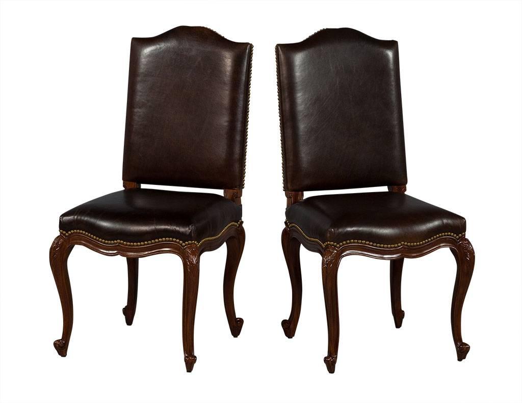 These French Louis XV style dining chairs are crafted out of a solid, curved wood frame and brown distressed leather seat and back, with brass studs on the back edge of the backrest and bottom edge of the seat. A truly Classic design, perfect for a