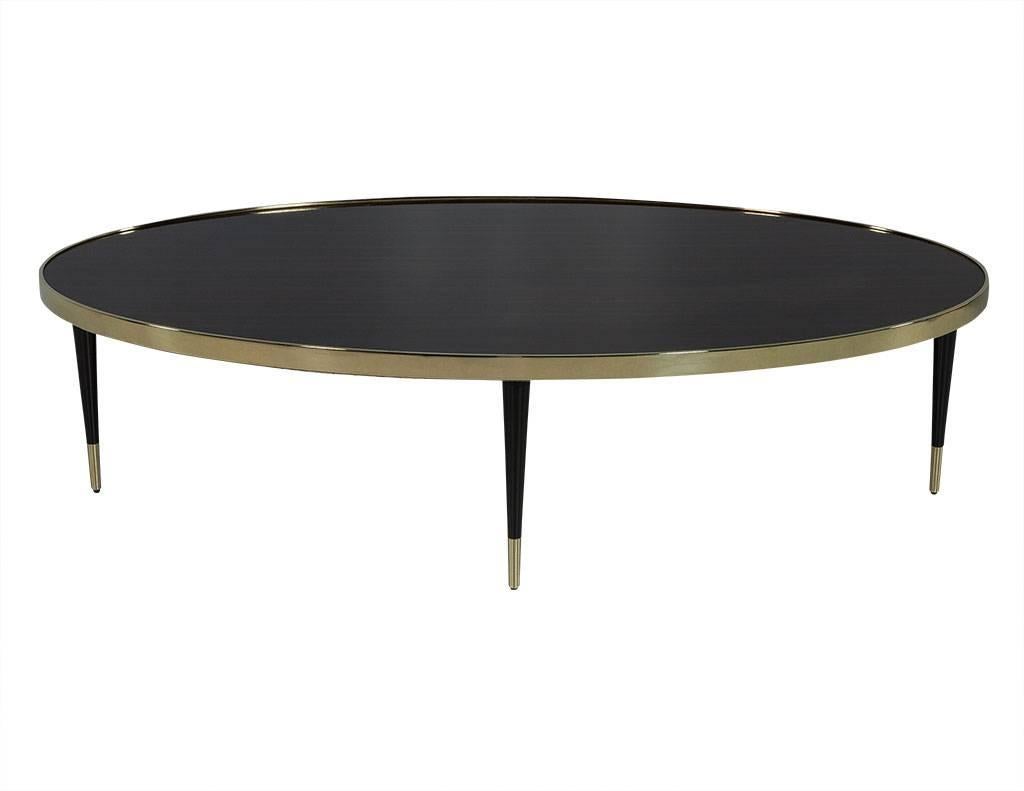 This modern style cocktail table is definitely well designed. The top is crafted out of oval ebony wood with a brass metal edge and sits atop tapered wood legs with bras tips. An ornate piece perfect for a luxe home.