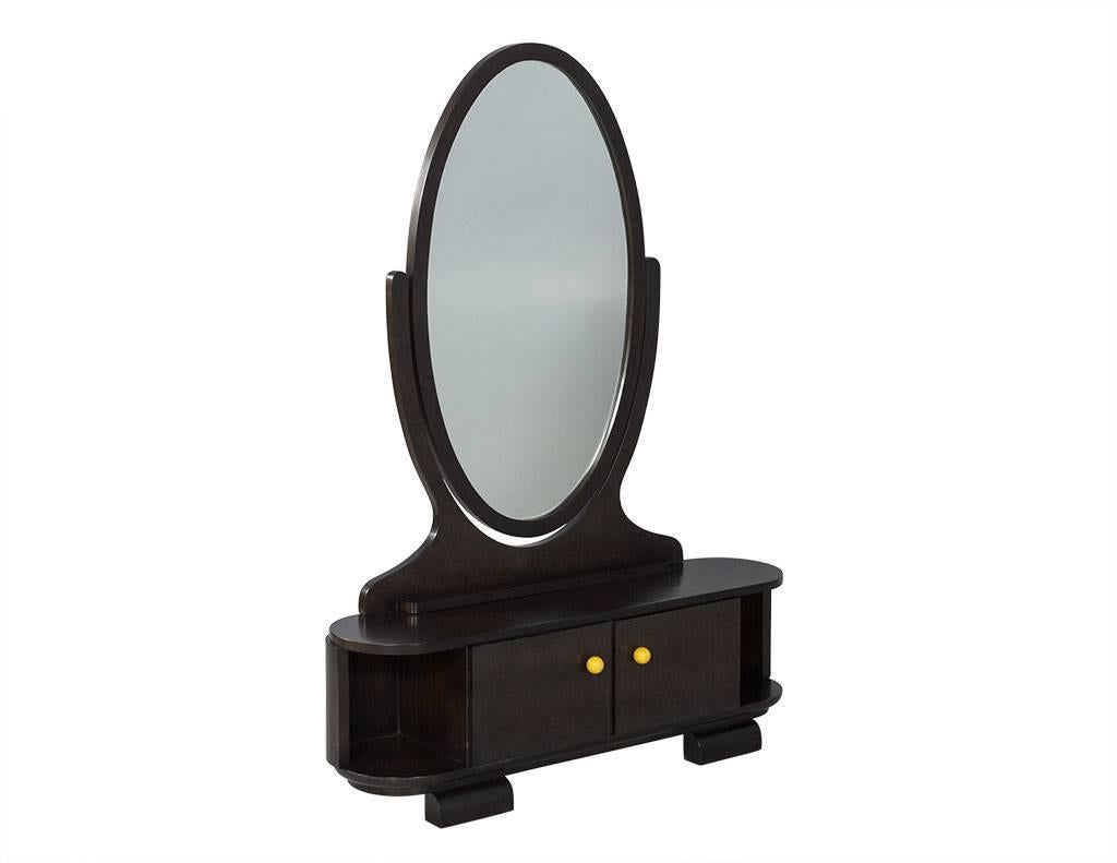 This Mid-Century Modern vanity is part of the Carrocel Revival collection. A vintage piece, the olive burl has been restored by our craftsmen to a rich espresso brown and is in excellent condition. Composed of a large, swivel oval mirror and a