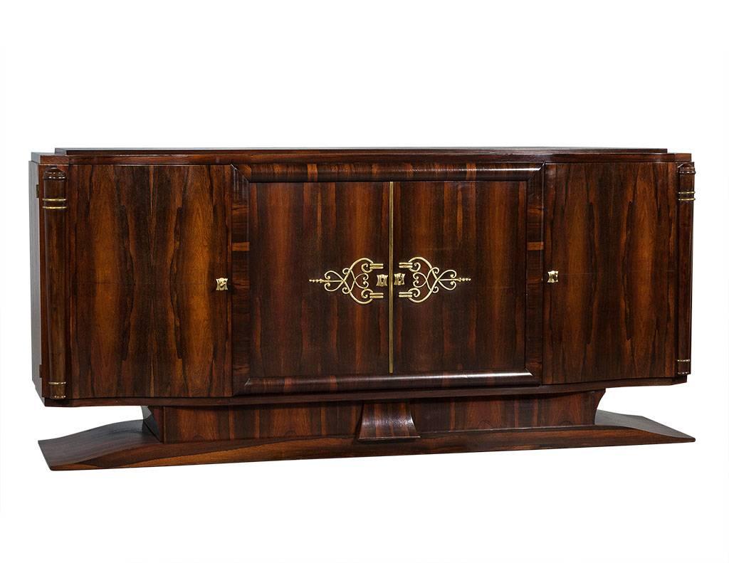 This Art Deco style sideboard buffet hails from France. It is truly a stunning work of art, crafted out of Macassar with solid brass keys, keyholes, and details on the two center doors. There are two drawers at the top inside, a shelf beneath for