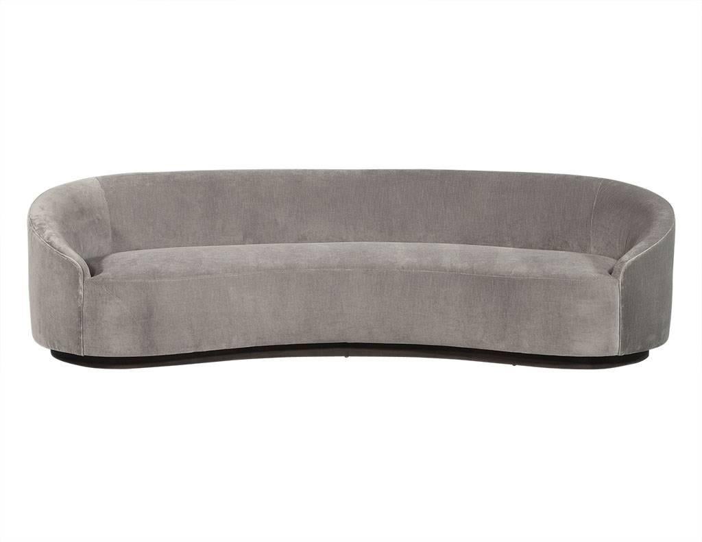 This modern sofa is perfectly plush and avant-garde. Upholstered in a pale grey velvet, this piece has a curved design with an inset dark wood base to match. Perfect for a comfortable living room.