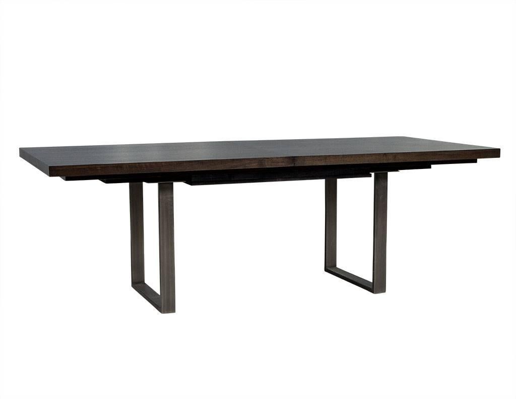 This modern dining table is a Carrocel custom piece. Crafted out of solid walnut with two leaves that are stored in the centre section, the piece sits atop two square-shaped metal bases to add contrast. Perfect for a fashionable home. Table is made