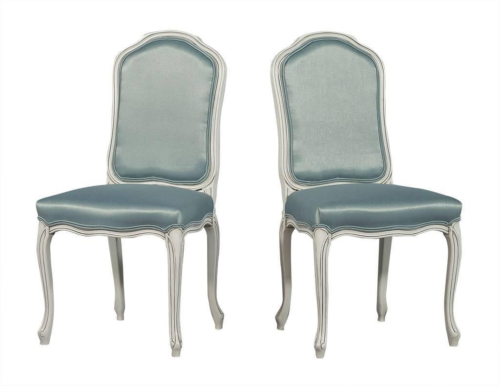 These Louis XV style dining chairs are made to order. Showcasing white antique painted frames with dark detailing and shading and pale turquoise satin fabric on the seat and both sides of the back, this set is perfect for a cottage style home.