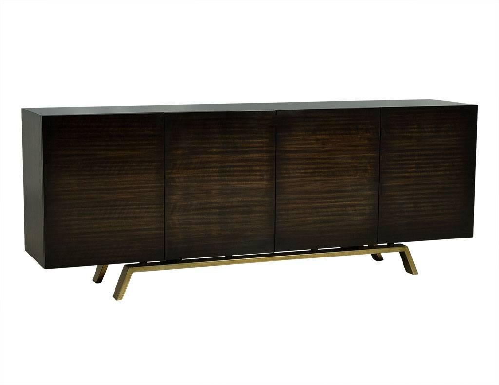 This modern sideboard buffet is made to order. The piece is finished in a glossy dark stain, and has four doors with three drawers on each end and three wider drawers front and centre. Sitting atop a complementary brass base with angled legs, this