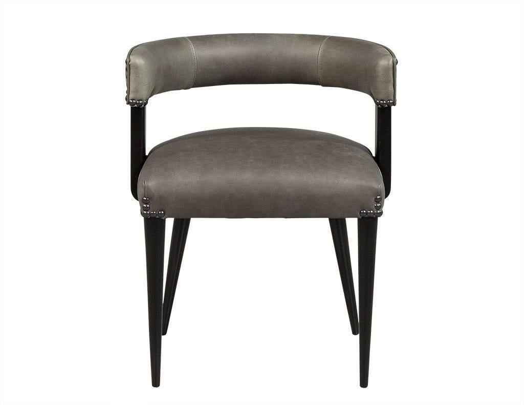 Original 1970s Mid-Century Modern design. These six grey leather dining chairs feature black finished wood legs and wide side panels supporting the curved armrest and backrest. Gun metal studs finish the sleek style.