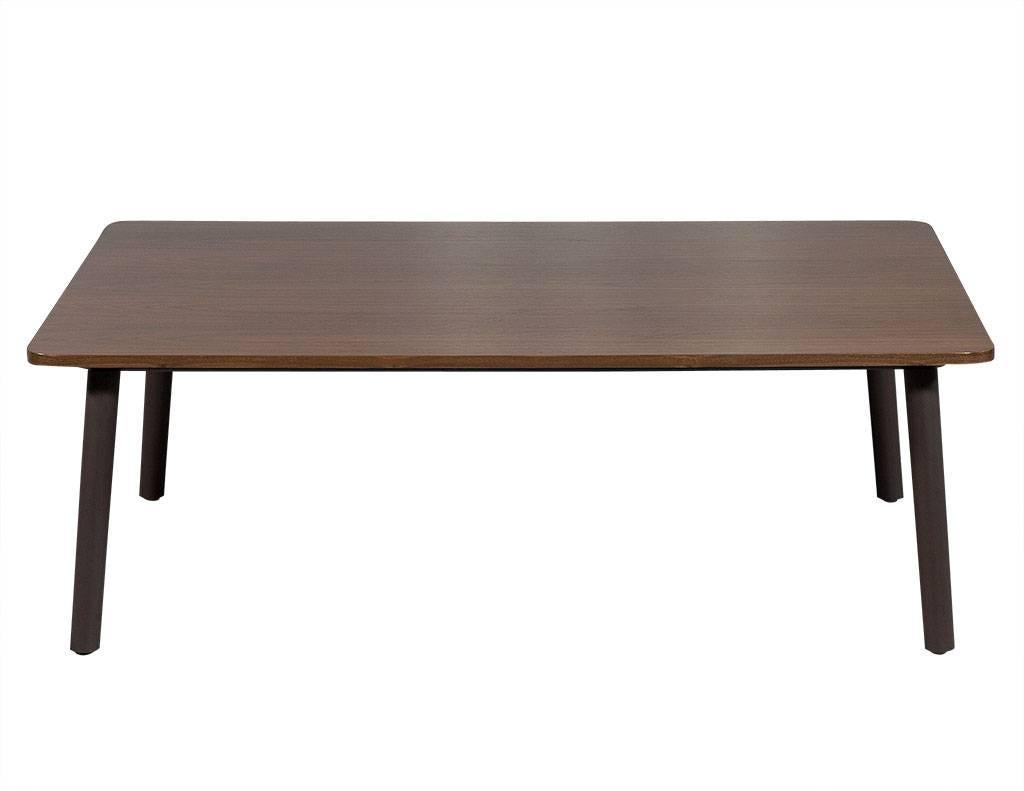 This Mid-Century Modern styled coffee table is custom-made and crafted out of solid walnut with rounded corners. It sits atop angled grey/brown legs with a matte finish. A striking piece perfect for a current living room!