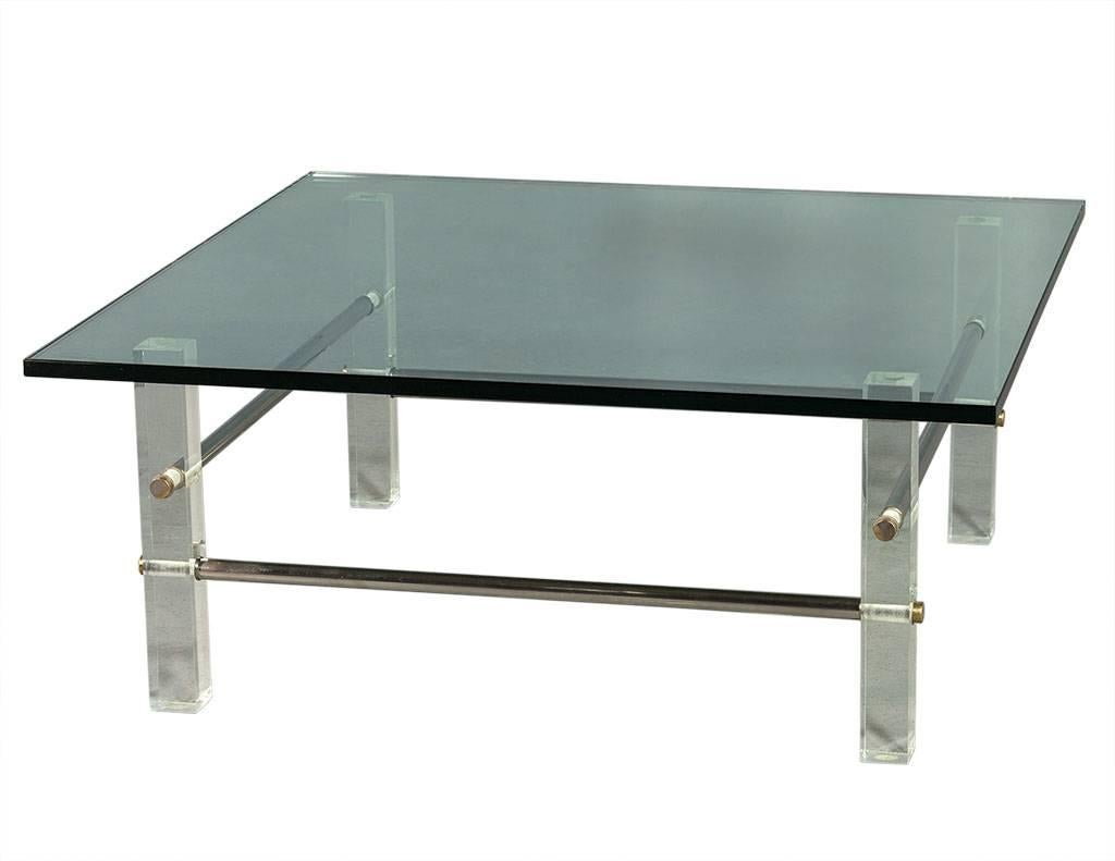 This modern coffee table is all original. The square top is crafted out of thick glass sitting atop square acrylic legs with round stainless-steel rod connectors. Perfect for a retro-inspired home!
