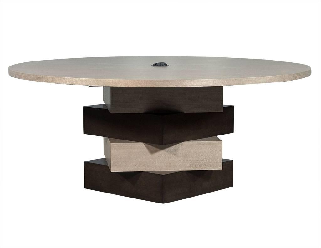 This unique dining table is modern in design, sporting a circular top positioned on a base of twisted multi-layered set of boxes. The top and base are coated in contrasting light and dark brown finishes, and the table has been outfitted with a