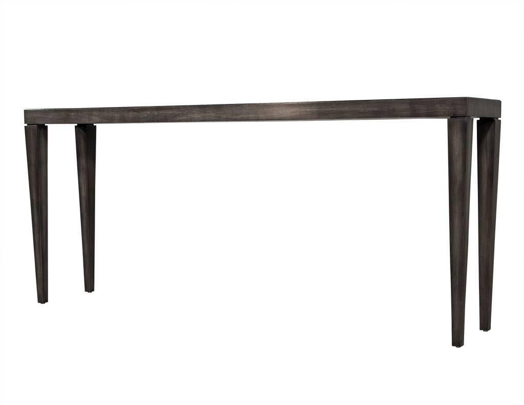 This elegant console table is finished in a hand-rubbed and polished grey stain, with tapered legs and a rectangular top. A sleek and modern piece, perfect for any stylish home.