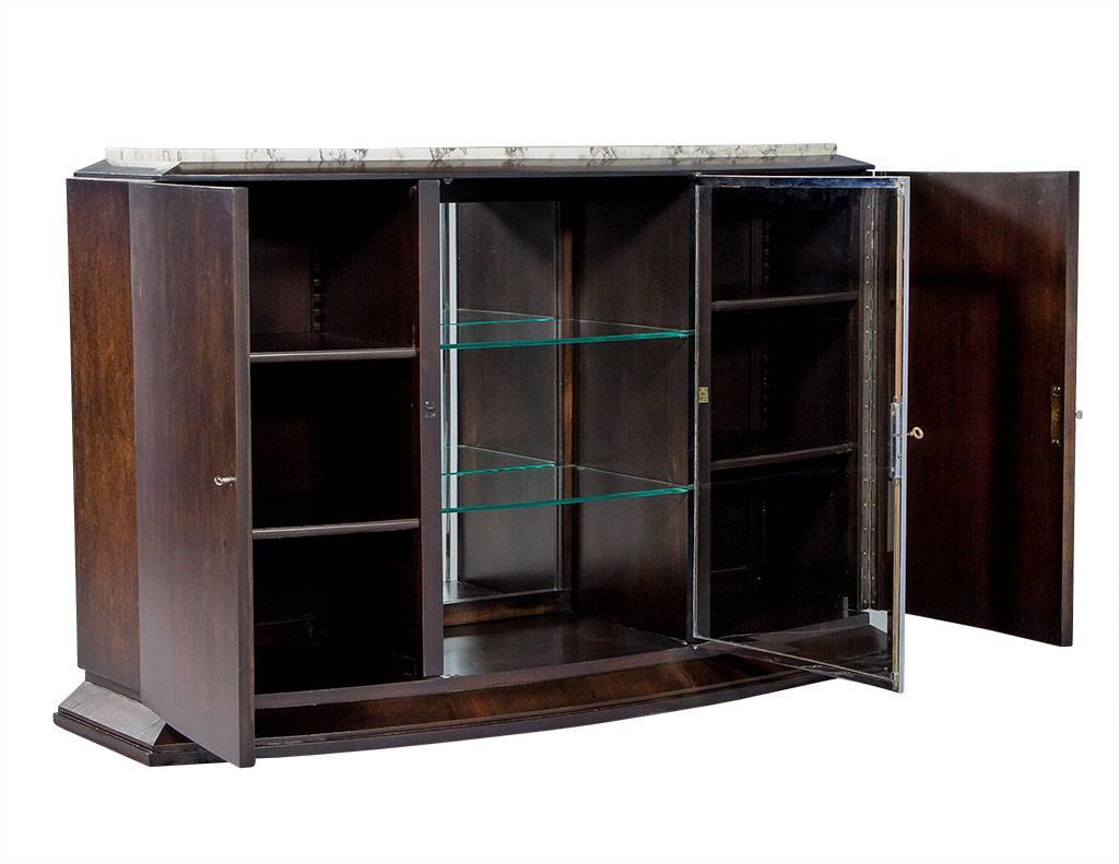 Gorgeous newly restored Art Deco bow front sideboard, enveloped in burled wood veneers. Original marble top with case divided into three lower shelved storage compartments, with the central compartment for display outfitted with glass shelves and a