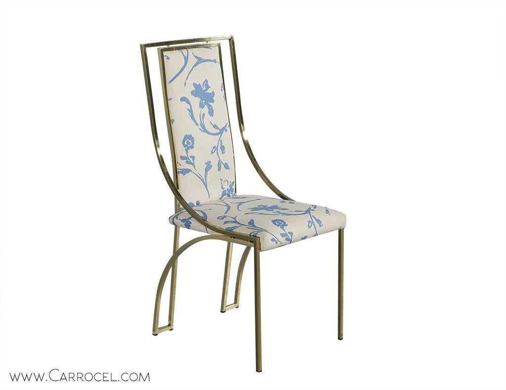 These sculptural chairs are designed of polished brass square bar contoured frames and upholstered in the original cream and blue colored floral patterned fabric. This glamorous set of chairs consists of four side chairs. The brass chair frames are