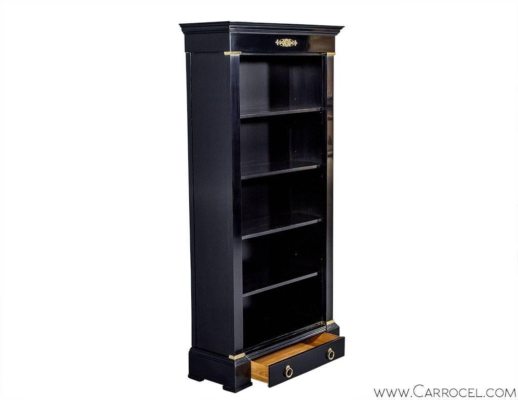 Vintage Baker Furniture mahogany black lacquer bookcase display. The interior is broken up into five shelves capped with molding and sitting on a base concealing a drawer. Bronze accents and hardware accent the hand polished black lacquer. This