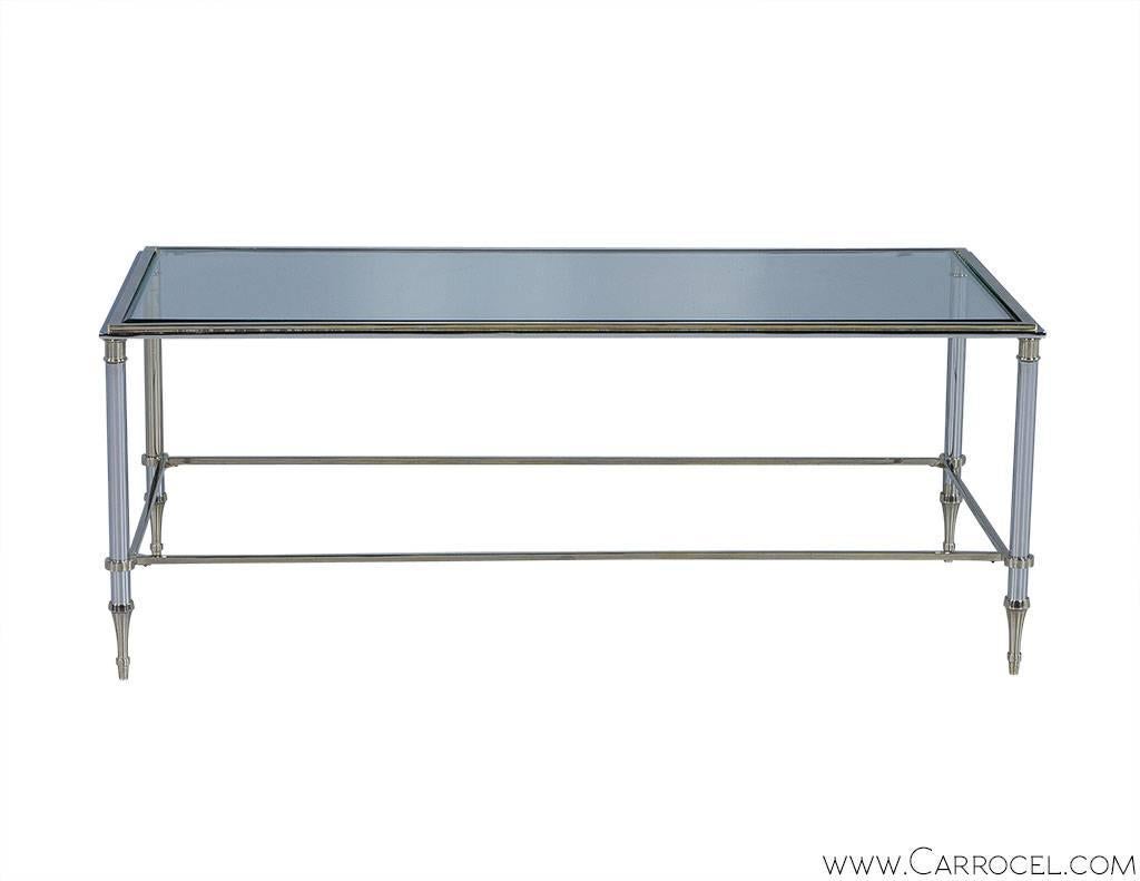 A sleek, delicate chrome and glass cocktail table with a relaxed elegance typical of Transitional furniture. A simple design consisting of four circular tapering  legs with ties, supporting a frame with a clear glass top, is accented by spade feet,
