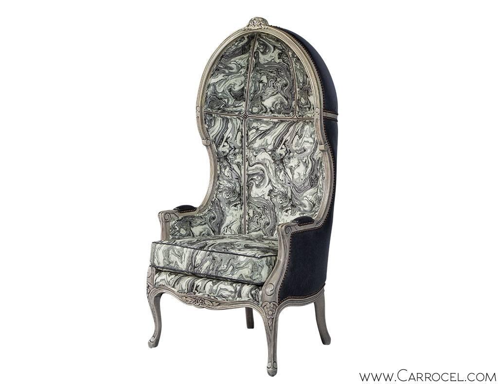 The classic Louis XV porter chair is designed with an avant-garde sentiment. The chair features a stunning monochromatic marbled upholstery interior and is grounded by a complimenting exterior of lightly distressed black Italian leather trimmed in