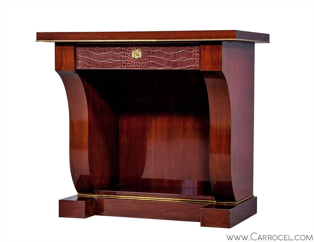 As an item in the Ralph Lauren Brook Street Collection, this nightstand was designed to be a 1940s classic revival piece. The features are a single croc embossed drawer with laurel wreath escutcheon hardware, a harp-shaped pedestal on a plinth base