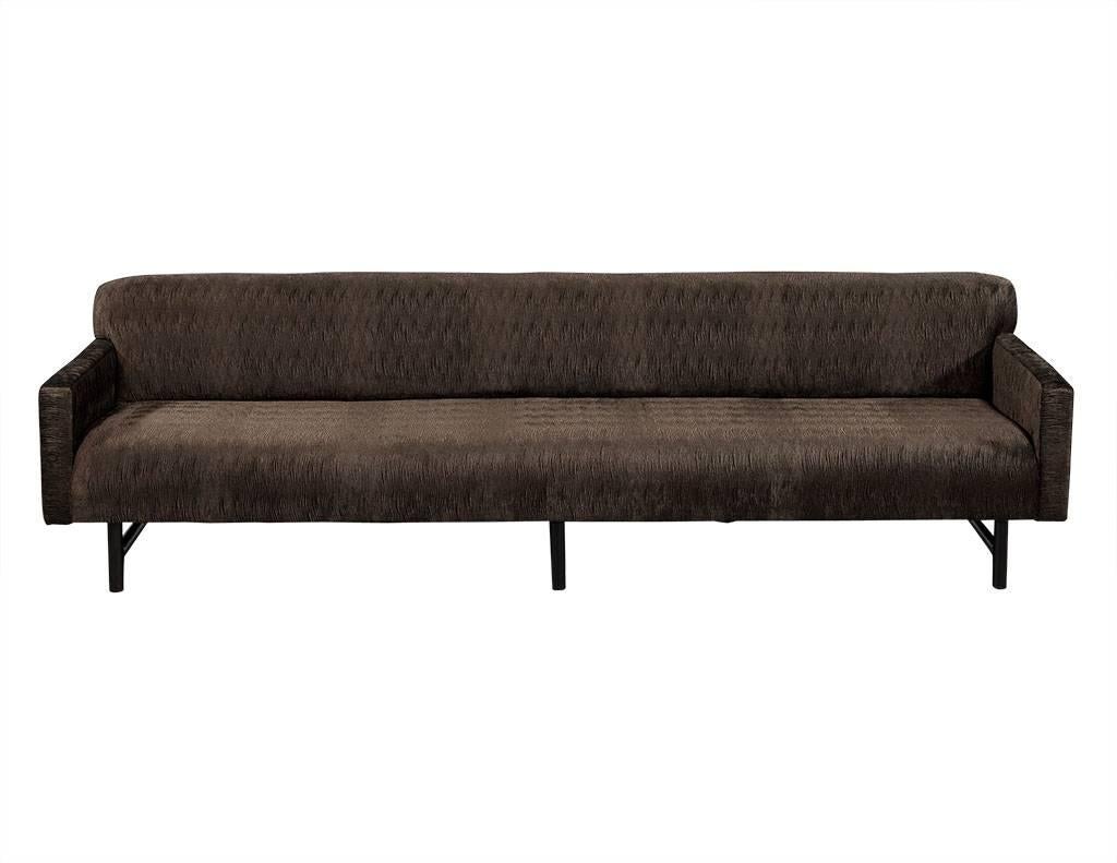 This midcentury style sofa features a wide and low profile frame, the piece is newly upholstered in luxurious dark taupe “wavy velvet” fabric. Sitting atop a black wooden base consisting of six legs (three sets of two) this piece is the perfect