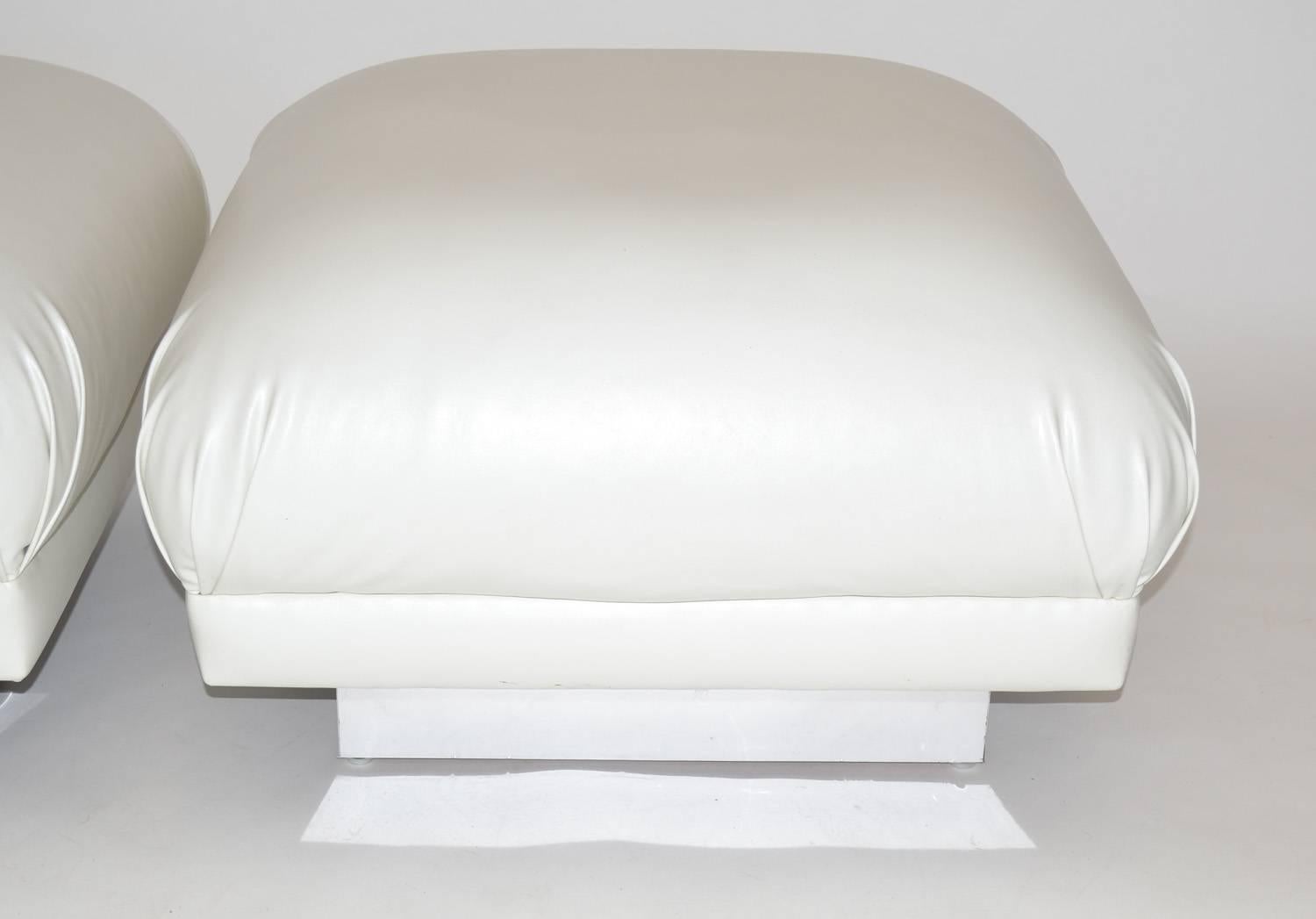 Pair of oversized ottomans or poufs in the soufflé style. Features large square cushions with pleated corners over a chrome banded wood base. Upholstered in white leatherette vinyl, 1970s.