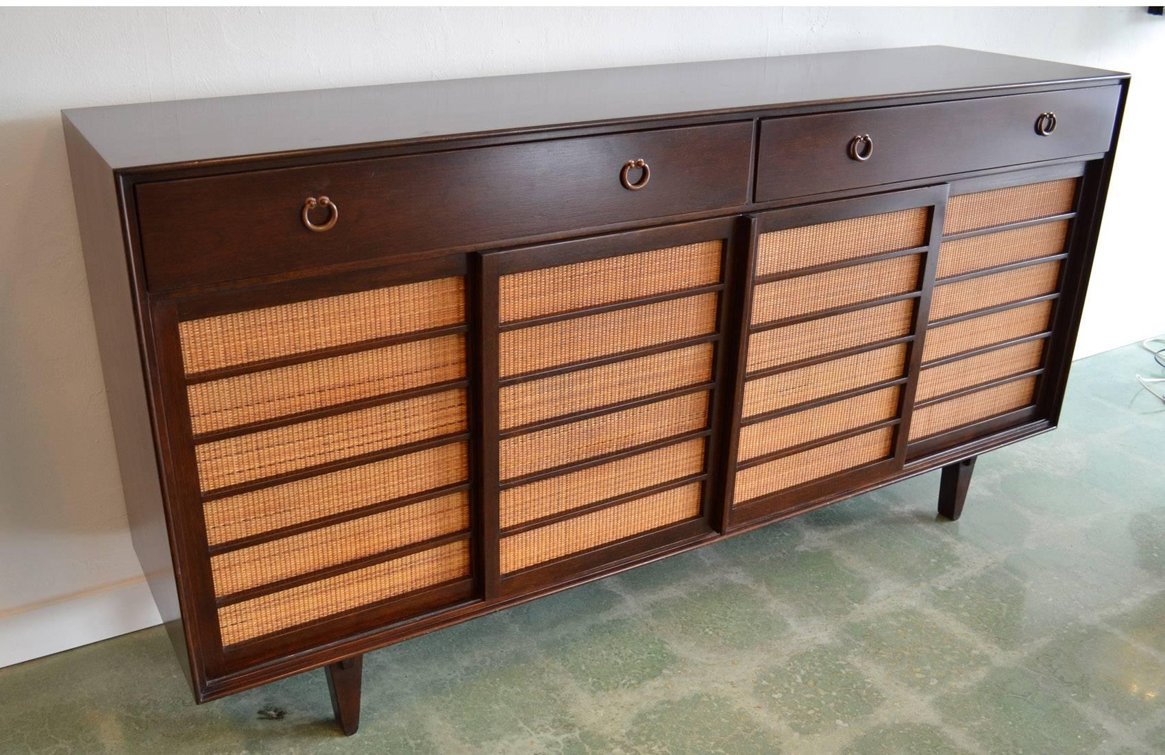 Sideboard credenza for Dunbar designed by Edward Wormley Mid-Century Modern grass front 671-A. Japanese-inspired in walnut with grass-covered sliding doors opening to pull-out and partitioned drawers with bronze pulls on exposed joinery legs.