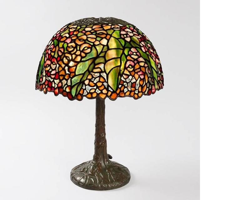 A Tiffany Studios New York "Pony Begonia" leaded glass and bronze table lamp, featuring a shade of mottled pink and red glass depicting blossoms of begonia, striated green for leaves, against a pale ground atop a miniature tree trunk base.