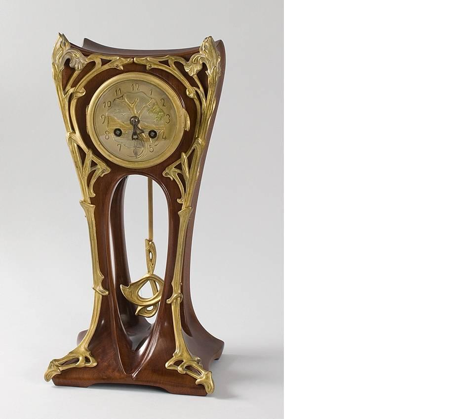 A French Art Nouveau Mahogany, gilt and enameled bronze clock featuring irises and a seaside scene by Louis Majorelle. Accompanied by one large and two small keys.  Circa 1900. 

A similar clock is pictured in: Louis Majorelle: Master of Art Nouveau