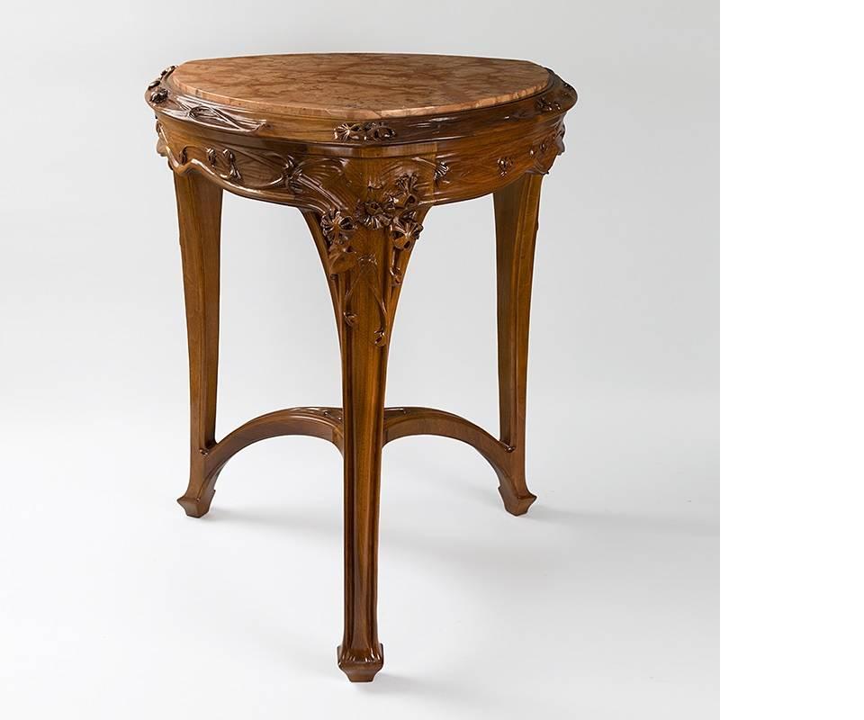 A French Art Nouveau marble top guéridon by Louis Majorelle. The legs, apron and cross piece of this triangular table are carved with flowers, vines and leaves. Fashioned of marble and carved and molded mahogany, the Chevrefuille guéridon's