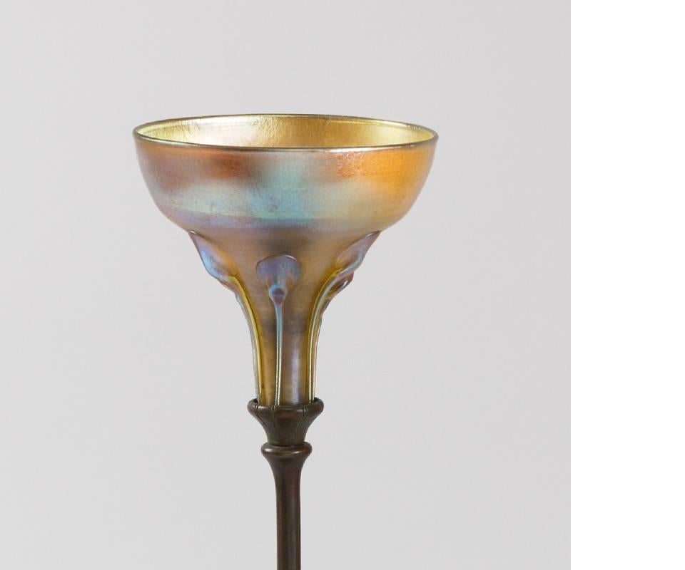 A Tiffany Studios New York patinated bronze and Favrile glass “Queen Anne’s Lace” candlestick.  The foot of the candle stick is ornately sculpted to look like a Queen Anne’s Lace flower. The candlestick is crowned with a blown gold iridescent 