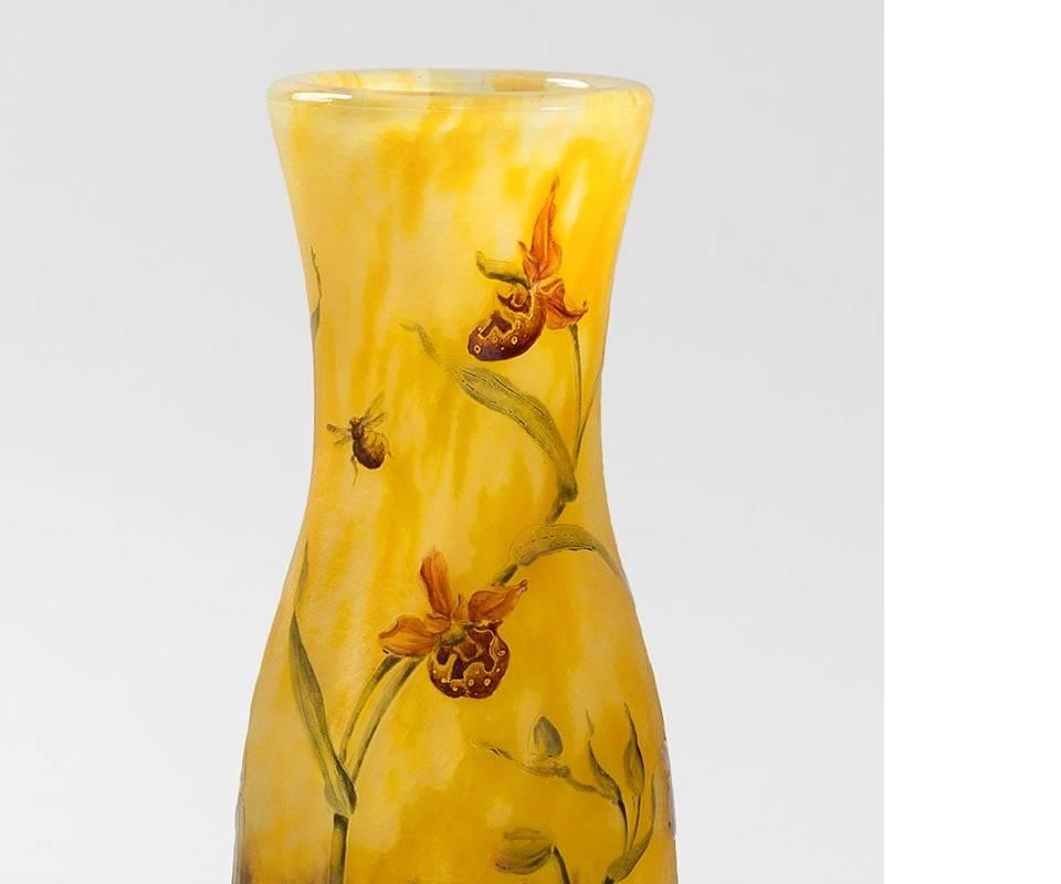 Ce vase en verre émaillé et gravé de Daum Nancy est une scène lumineuse est dominée par deux plans de verre tacheté, jaune d'or sur un violet profond, qui ensemble créent un paysage. Le vase est décoré d'orchidées gravées et émaillées. Les orchidées