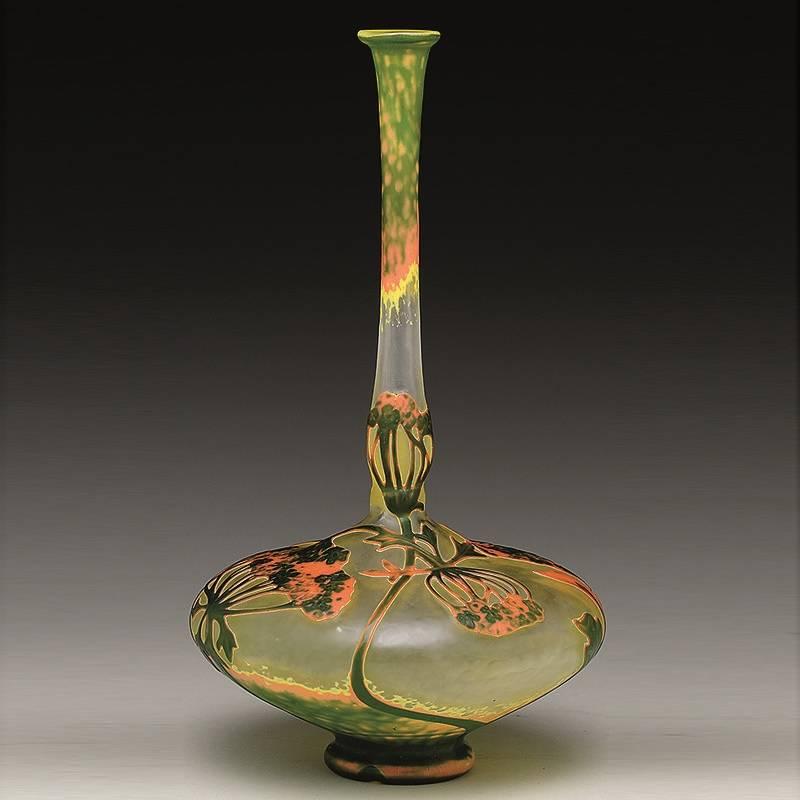 A French Art Nouveau cameo glass vase by Daum Nancy. The body of the vase is decorated with orange flowers with carved green centers on green stems that climb part-way up the elongated neck. The top of the neck is decorated in mottled yellow, green