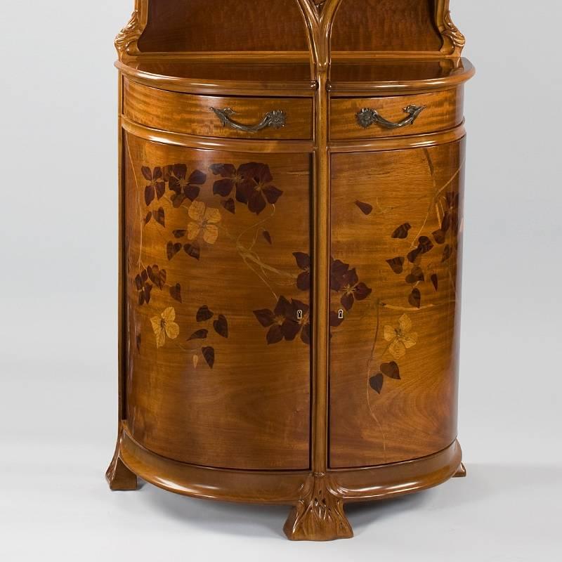 A French Art Nouveau walnut vitrine  in ash and rosewood, featuring clemantis depicted in marquetry and deep carving. The vitrine has two lockable storage areas, each with a shelf, and two drawers that swing out from the body. There is also a shelf