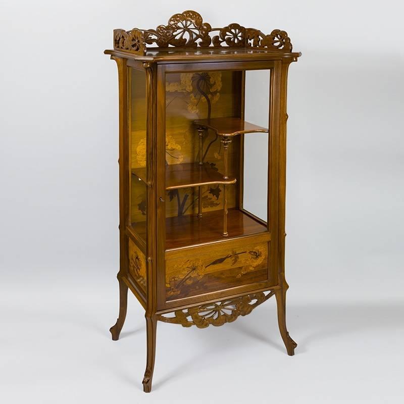 A French carved and fruitwood marquetry inlaid Ombelliféres vitrine by Emile Gallé. The vitrine has marquetry ombelle flowers in its interior and on the panel below the bottom shelf. The interior has two small carved half shelves. The top and bottom
