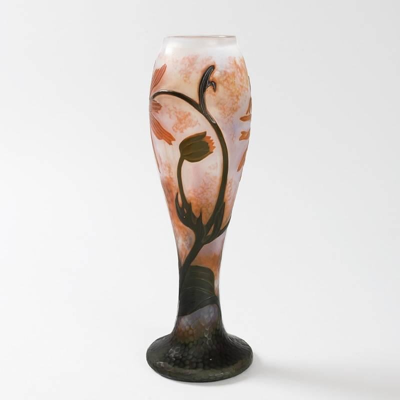 A French Art Nouveau cameo glass vase by Daum, featuring a scene of red blooming flowers on an opaque white martelé ground. The flowers, which have dark centers, are suspended from dark curving stems that emerge from dark green carved leaves, circa