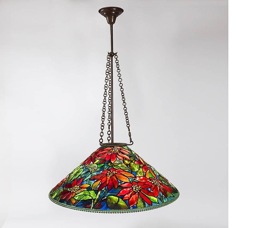 A Tiffany Studios New York glass and bronze “Poinsettia” chandelier, featuring a leaded glass shade depicting deep red and mottled pink poinsettia flowers and mottled green leaves against a green and blue hued ground. This highly unusual shade does