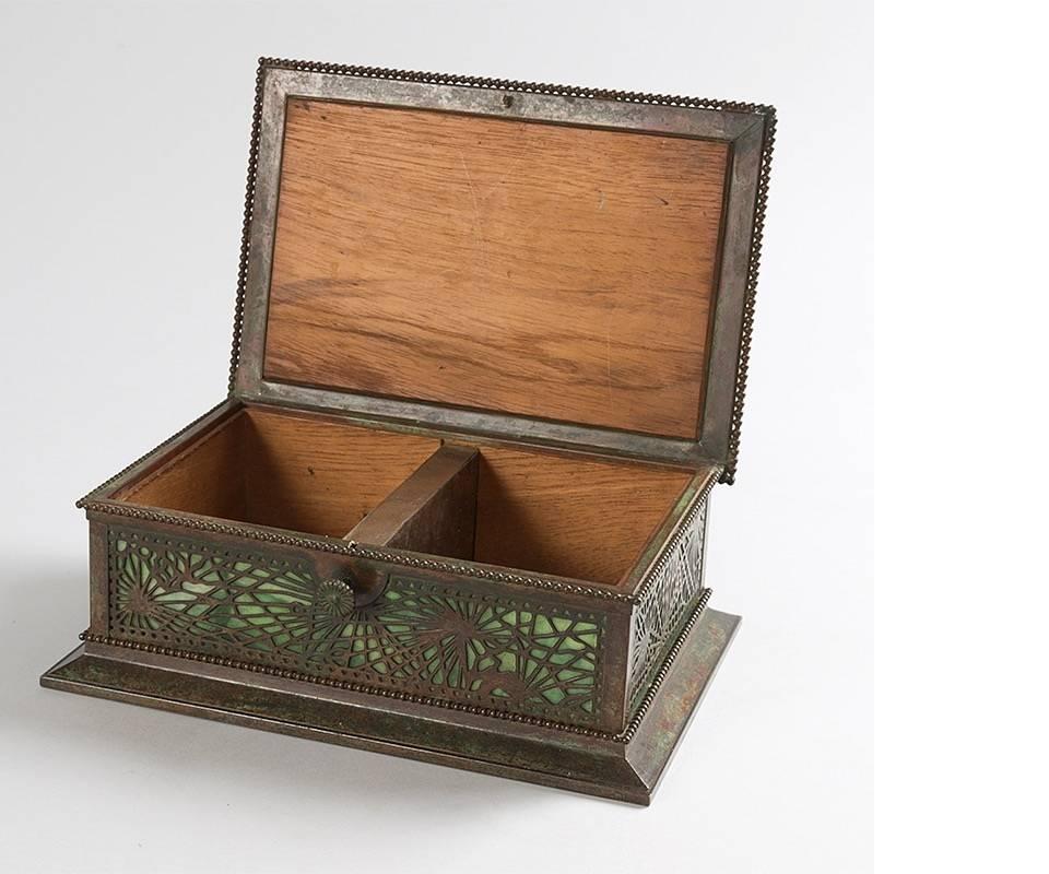A “Pine Needle”  cigar box by Tiffany Studios New York.  This bronze box has a pierced pine needle pattern overlaid on green slag glass, beaded borders around the edges, splayed beveled base, hinged lid with lock and a cedar lined interior with