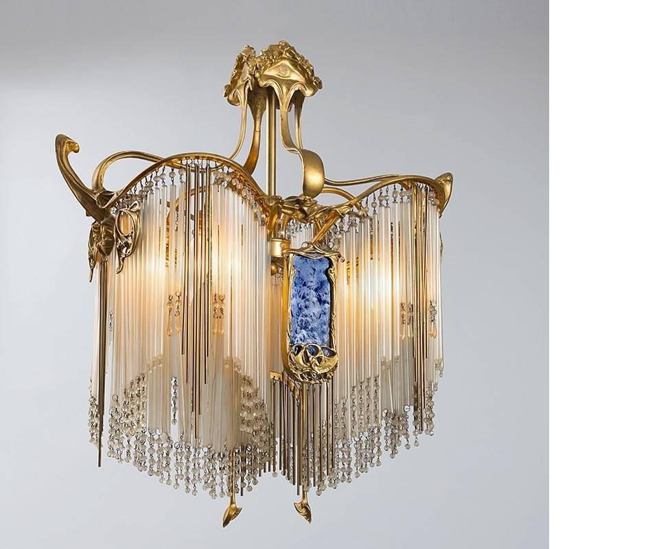 A French Art Nouveau gilt bronze and glass chandelier from the Lustre Lumière collection by Hector Guimard. The body of this chandelier is made of gilt bronze that is crafted into a curved, semi-ovular frame. This top section of the hanging light