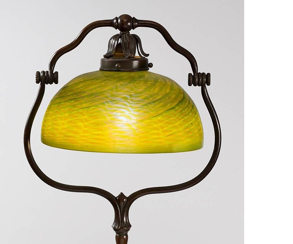 A Tiffany Studios New York patinated bronze and Favrile glass harp floor lamp. The lamp features a green Damascene shade with iridescent decoration suspended within a harp base, circa 1900.

Similar base and shade are pictured separately in: